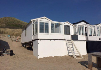 Strandhaus 'Dishoek 345/346' mit weißer Fassade und Glasveranda, gelegen auf Sand am Fuß einer Düne.