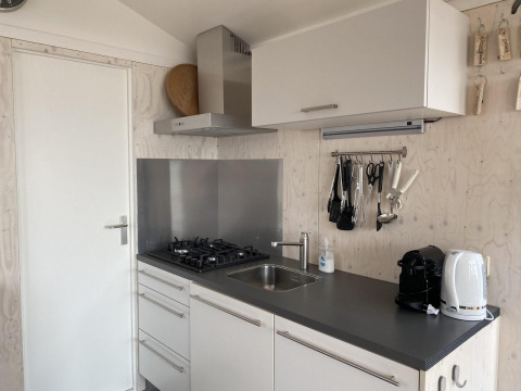 Cocina moderna de cabaña con estufa de gas, fregadero, cafetera y hervidor en Beach house 'Dishoek 345/346', Zeeland.