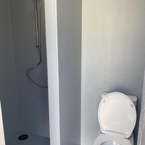 Et badeværelse i en hytte med et bruseområde til venstre og et toilet til højre, alt i lyse farver.