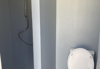 Et badeværelse i en hytte med et bruseområde til venstre og et toilet til højre, alt i lyse farver.