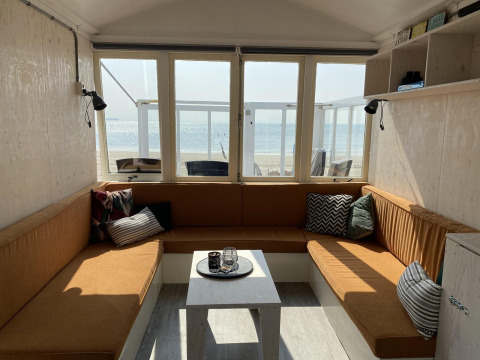 Knusse woonkamer in een strandhuis met grote ramen, zicht op zee en moderne zithoek te Dishoek, Zeeland.