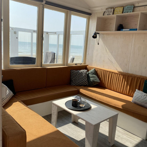 Salon confortable dans une cabane de plage à Dishoek, Zeeland, avec canapés bruns et vue sur la mer.
