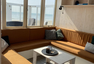 Salon confortable dans une cabane de plage à Dishoek, Zeeland, avec canapés bruns et vue sur la mer.