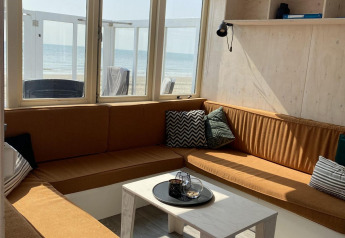 Hyggelig stue med brune sofaer, hvide borde og udsigt til stranden fra et strandhus i Dishoek, Zeeland.