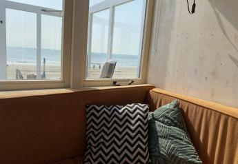 Sofá esquinero con cojines y vista a la playa en Beach house 'Dishoek 345/346' en Zeeland, Países Bajos.