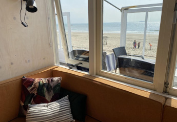Vista desde una cabaña con sofá marrón y cojines hacia la playa y el mar en Dishoek, Zeeland, Países Bajos.