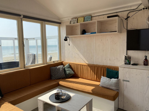 Sala luminosa en casa de playa con vista al mar, sofá esquinero y decoración acogedora en Zeeland, Países Bajos.