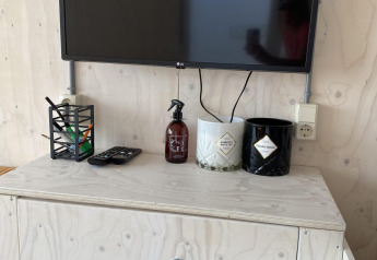 TV-skærm, fjernbetjening, sprayflaske og krukker på lyst træskab i Beach house Dishoek 345/346, Zeeland.