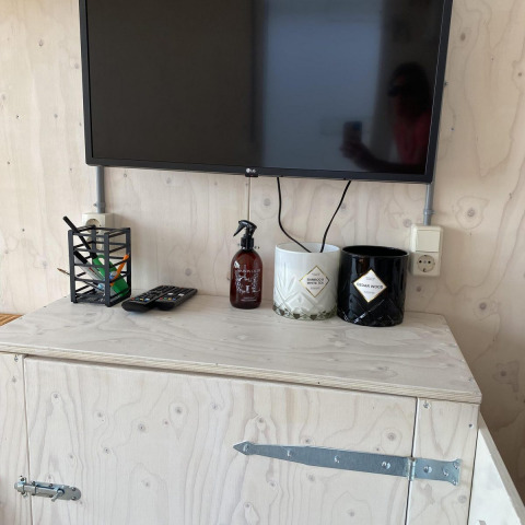 TV, afstandsbedieningen, spray en decoratieve potten op licht houten kast in Beach house Dishoek 345/346, Zeeland.