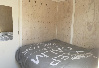 Dormitorio en una cabaña de madera con cama doble y ropa de cama gris en Beach house 'Dishoek 345/346'.