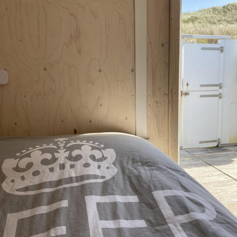 Vista del dormitorio en Beach House Dishoek 345/346 con ropa de cama, puerta abierta y dunas fuera.