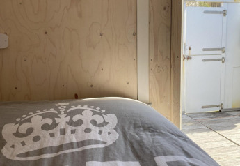 Vista del dormitorio en Beach House Dishoek 345/346 con ropa de cama, puerta abierta y dunas fuera.