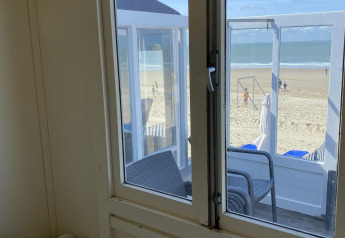 Udsigt gennem et vindue i en strandhytte over Dishoek-stranden i Zeeland, Holland, med havet i baggrunden.