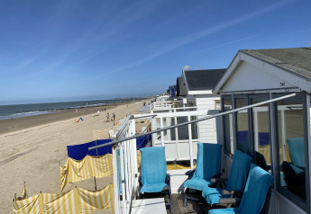Case sulla spiaggia con sedie blu e frangivento gialli sulla sabbia di Dishoek, Zeeland, Paesi Bassi.