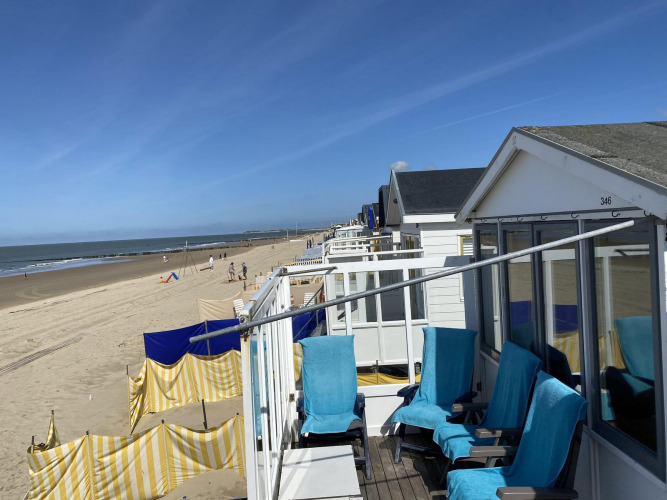 Strandhäuser mit blauen Stühlen und gelb-weißen Windschutzen am Sandstrand in Dishoek, Zeeland.