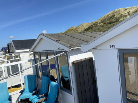 Strandhytter ved Dishoek med blå himmel, sandklitter og udendørs stole dækket med blå håndklæder.