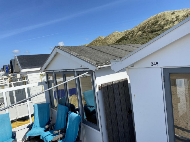 Strandhuisjes in Dishoek, Nederland, met duinen op de achtergrond en blauwe stoelen voor de deur.