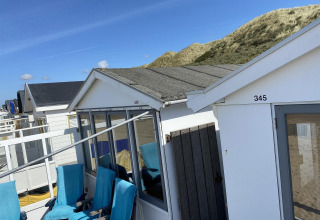 Strandhuisjes in Dishoek, Nederland, met duinen op de achtergrond en blauwe stoelen voor de deur.