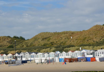 Strandhäuser am Sandstrand von Dishoek, Zeeland, Niederlande, mit Dünen und blauem Himmel im Hintergrund.
