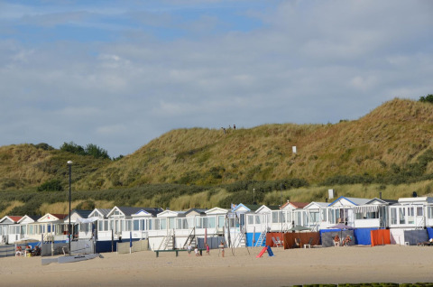 Strandhytter ved sandklitter i Dishoek, Zeeland, Holland med folk, blå himmel og grønt landskab.