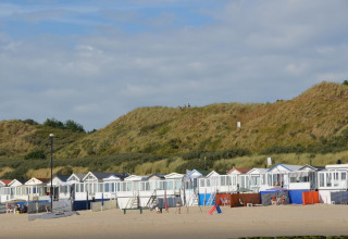 Strandhytter ved sandklitter i Dishoek, Zeeland, Holland med folk, blå himmel og grønt landskab.