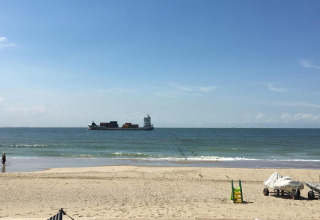 Strandudsigt fra Beach house 'Dishoek 345/346' med sand, hav, containerskib og både i Zeeland, Nederlandene.