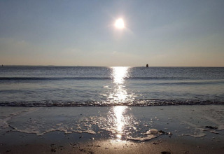 Solnedgang over havet ved Dishoek Beach House i Zeeland, Holland med bløde bølger og roligt vand.