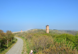 View of green dunes, a winding path, and two striped towers at Dishoek beach in Zeeland, Netherlands.