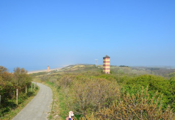 Vista de dunas verdes, camino y dos torres rayadas en la playa de Dishoek, Zelanda, Países Bajos.