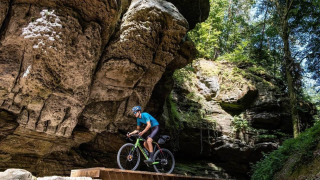 Ciclista cruza un puente de madera bajo grandes rocas en Camping du Rivage en Diekirch, Luxemburgo.