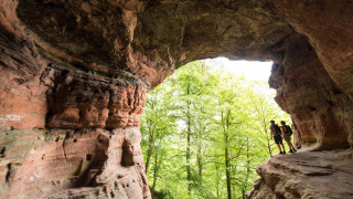 Dos excursionistas exploran una gran cueva con vistas a árboles verdes en Diekirch, Luxemburgo.