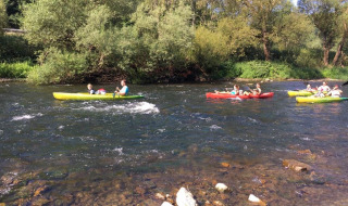People kayaking on a scenic river surrounded by trees at Camping du Rivage holiday park in Diekirch, Luxembourg.