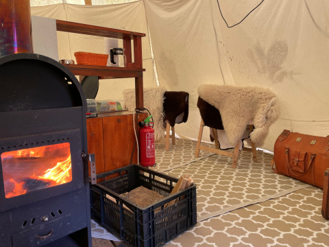Interior de tienda tipi en Buytenplaets Suydersee con estufa de leña, alfombra y sillas con pieles.