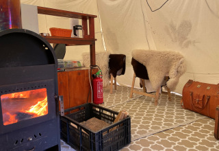 Intérieur d’un tipi à Buytenplaets Suydersee avec poêle à bois, tapis, chaises en peau, et extincteur.