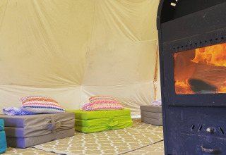 Intérieur d'une tente tipi à Buytenplaets Suydersee, Pays-Bas, avec matelas au sol et poêle à bois.