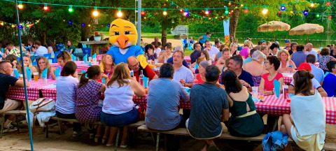 Menschen sitzen an langen Tischen mit rot-weiß karierten Decken auf Camping Paradis Aubeterre in Frankreich.