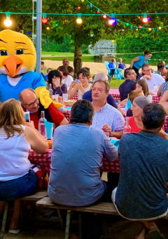 Personas reunidas en mesas largas con manteles rojos y luces en Camping Paradis Aubeterre, Francia.