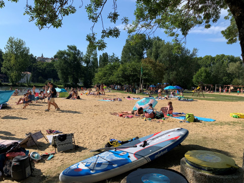 Turistas descansan en la playa de arena bajo árboles en Camping Paradis Aubeterre, Nouvelle-Aquitaine, Francia.