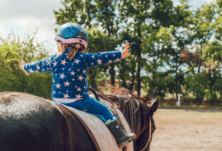 Un niño con casco azul monta a caballo cerca de Aubeterre sur Dronne, Francia, rodeado de árboles verdes.