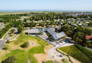 Vue aérienne d’un village de tiny houses avec espaces verts, aire de jeux et côte à l’arrière-plan.