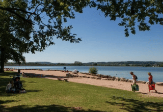 Menschen entspannen am See im Camping du Lac, einem Ferienpark in Grand Est, Frankreich, bei Sonne.