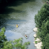 Two people paddle kayaks on a peaceful river surrounded by lush greenery near Villegusien le Lac, France.