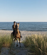 Persona montando a caballo en la playa frente al mar, foto tomada en un parque vacacional con glamping.