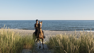 Persona montando a caballo en la playa frente al mar, foto tomada en un parque vacacional con glamping.