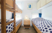 Helles Kabinenzimmer mit Etagenbett und zwei Einzelbetten, gepunktete Decken, Nachttisch und Fenster.