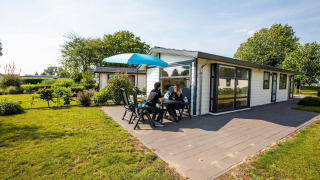 Dos personas sentadas al aire libre bajo una sombrilla en la cabaña Comfort en un día soleado y verde.
