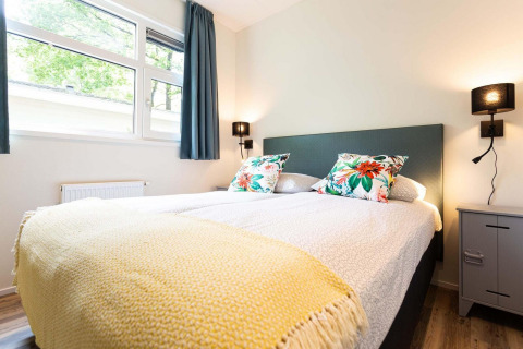 Heldere glampingkamer met knus bed, kleurrijke kussens, grote ramen en moderne verlichting.