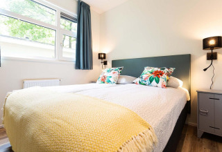 Lyst og moderne glampingværelse med komfortabel seng, farverige puder og store vinduer med udsigt.