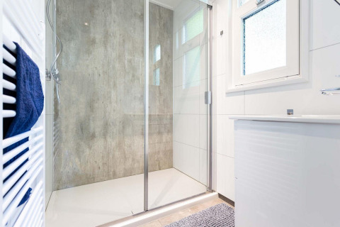 Moderne douche in een glampingverblijf met glazen deur, handdoekrek en groot raam voor licht.