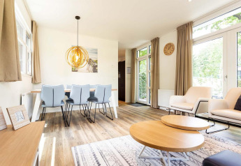Lyst glamping-ophold med moderne indretning, spisebord, komfortable stole og store vinduer mod haven.